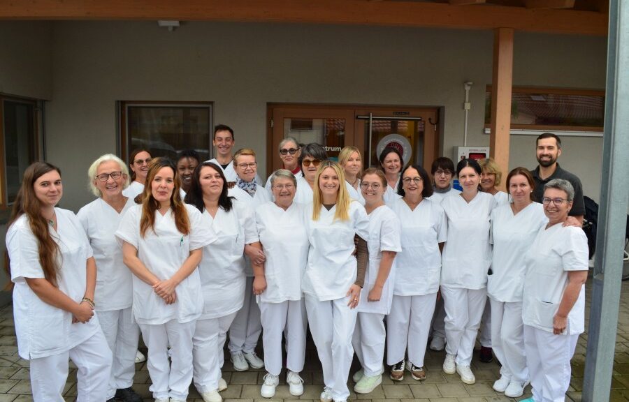 Team der ambulanten Pflege der Sozialstation Ried in weißer Berufskleidung vor dem Eingang der Station