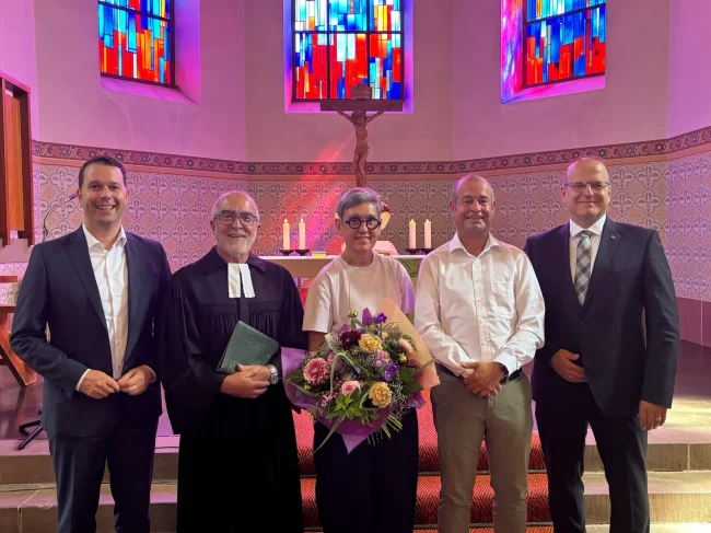Gruppe von fünf Personen steht in einer Kirche, eine Frau hält einen Blumenstrauß zur Verabschiedung