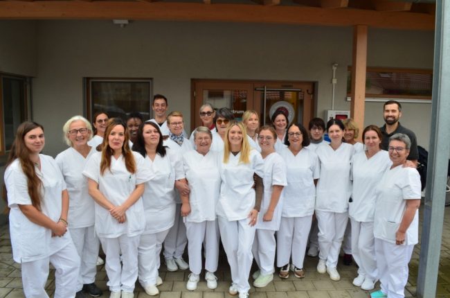 Team der ambulanten Pflege der Sozialstation Ried in weißer Berufskleidung vor dem Eingang der Station